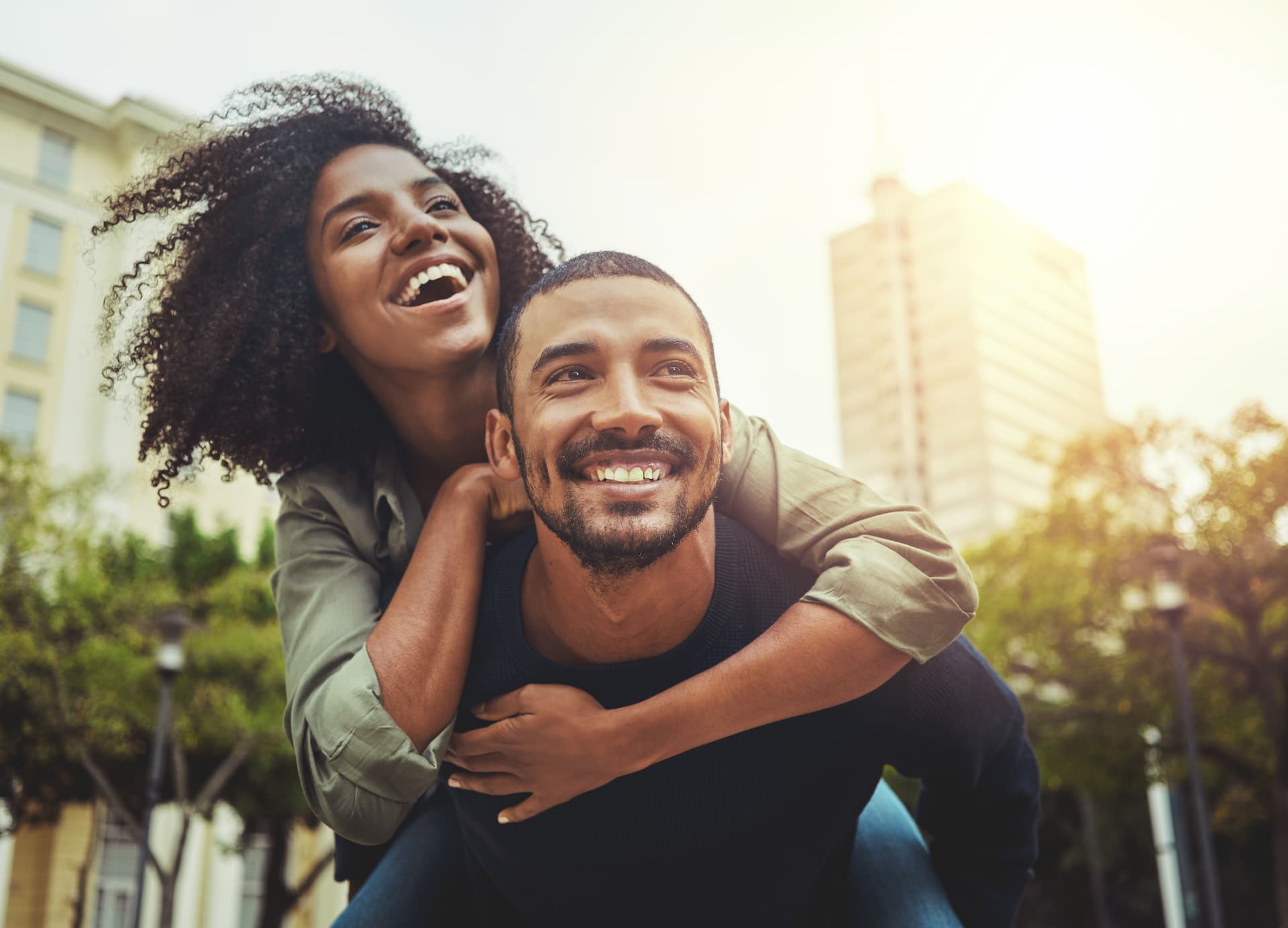 A young happy couple where a man is giving a woman a piggyback ride in the city